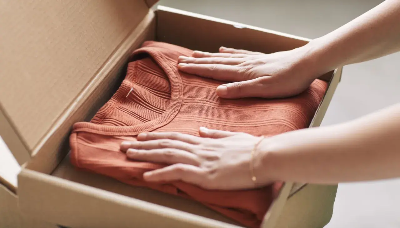 Mani che accarezzano una maglietta color terracotta appena arrivata, pronta per il primo lavaggio per fissare i colori.