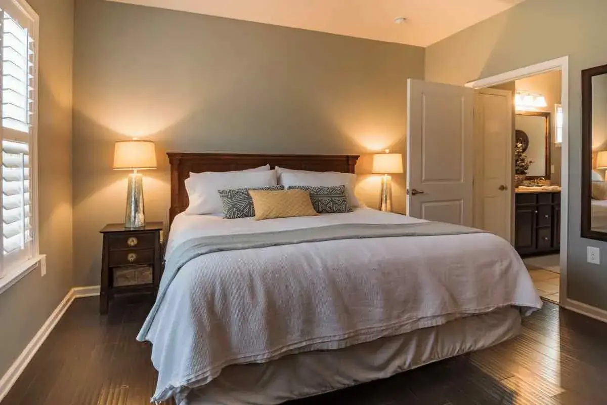 Accogliente camera da letto colori caldi, con letto king size, comodini con lampade e porta aperta su un bagno.