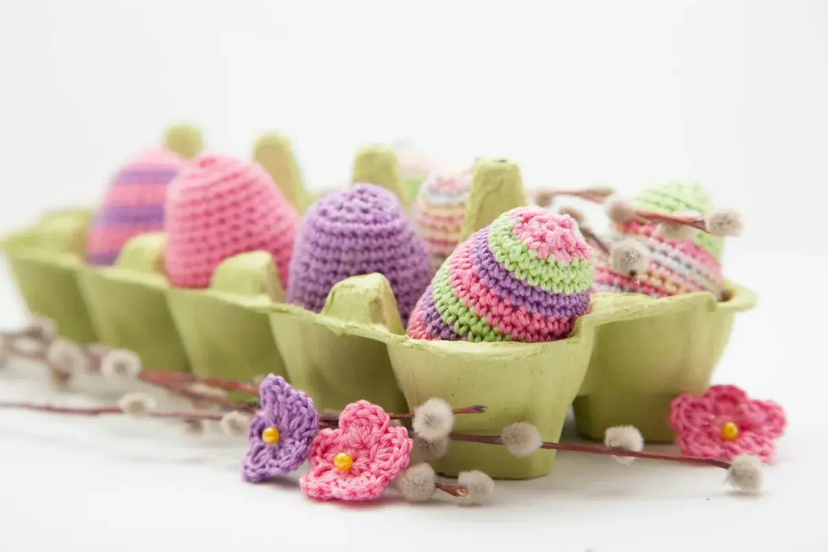 Uova di Pasqua all'uncinetto in lana colorata, perfette per lavoretti di Pasqua creativi. Fiori e ramoscelli di salice completano la scena.