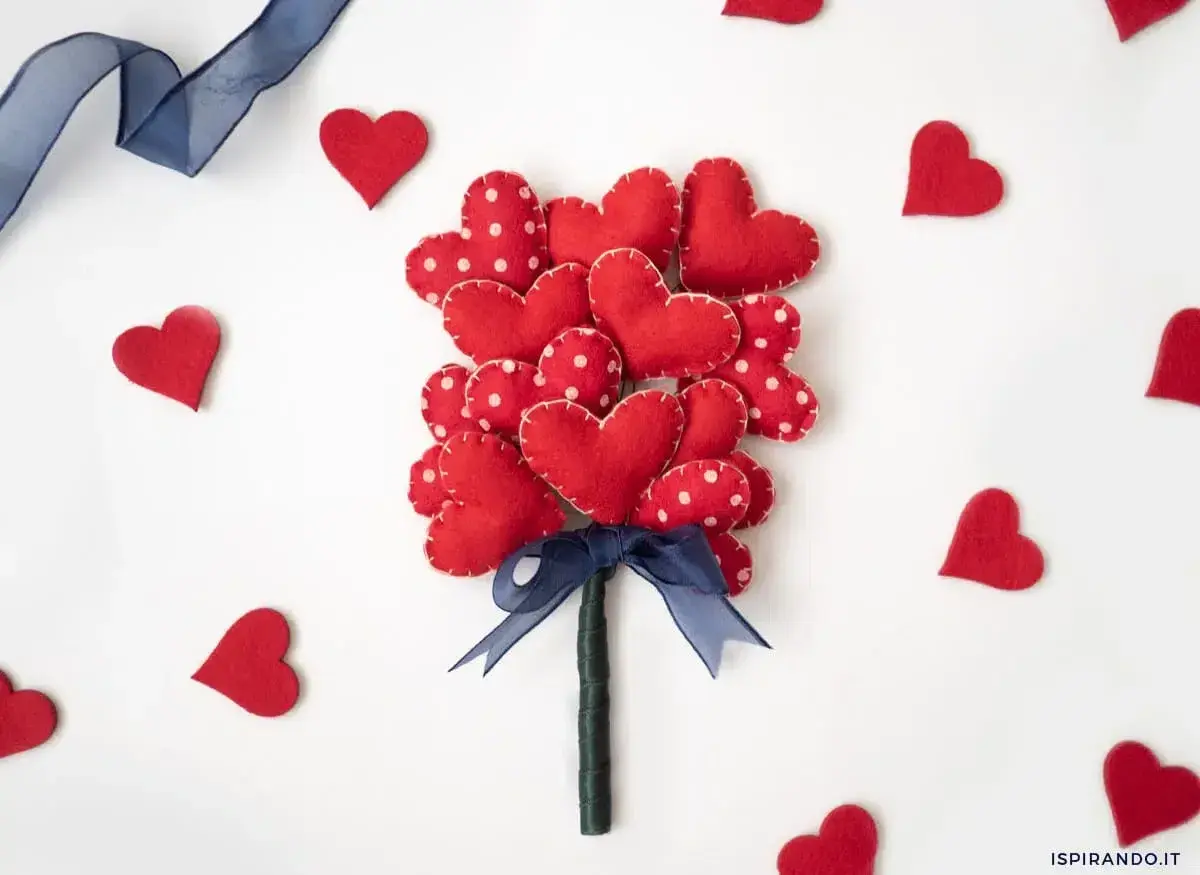 Un bouquet di cuori rossi in feltro, perfetti per regali fai da te San Valentino. Un nastro blu lega il tutto, circondato da cuoricini sparsi.