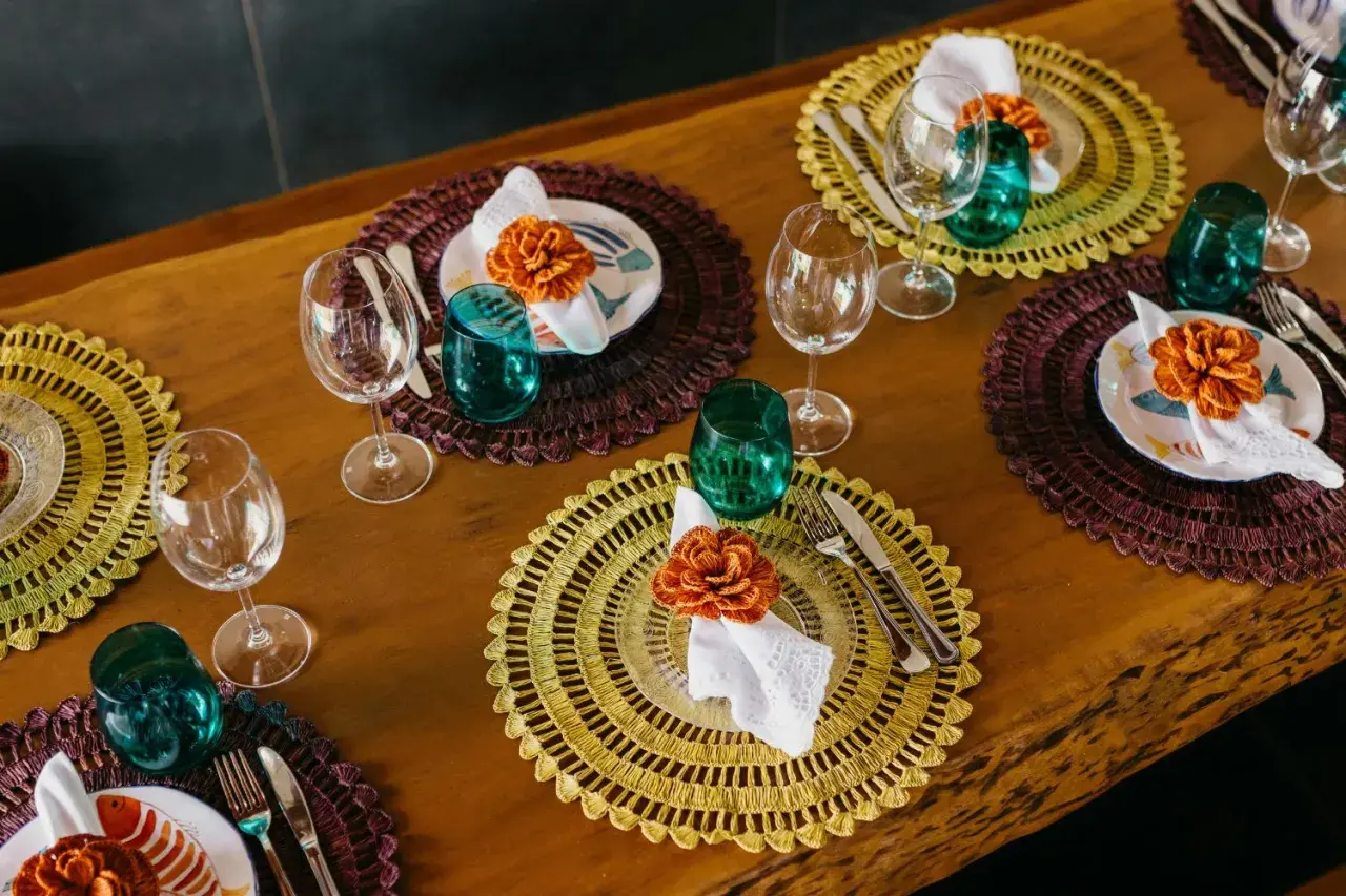 Sottopiatti eleganti fai da te con decorazioni floreali arancioni, bicchieri verdi e posate su un tavolo di legno.