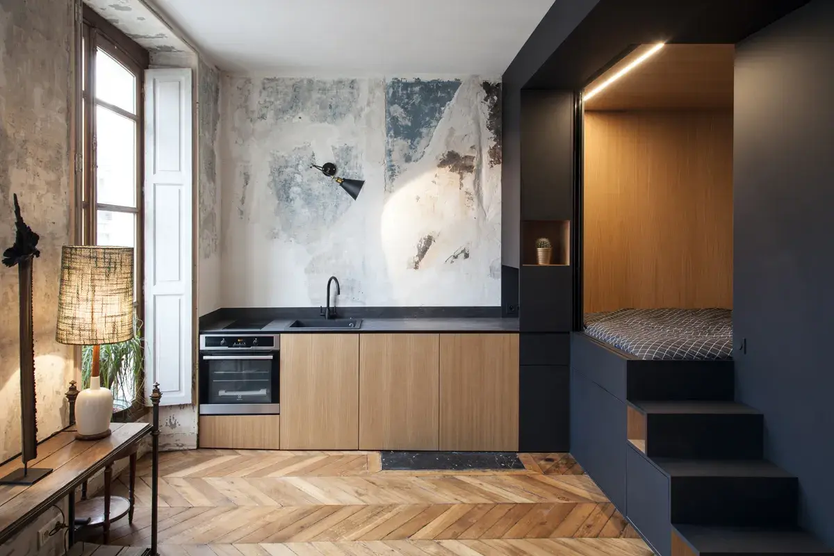 Cucina moderna con letto a soppalco, un esempio di idee arredo casa piccola. Pareti grezze, mobili in legno e dettagli industriali.