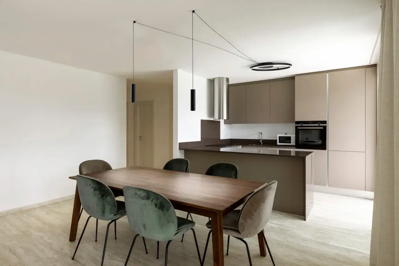 Un lampadario decentrato con cavi sottili illumina un tavolo da pranzo in legno con sedie verdi. Soluzioni moderne per un ambiente elegante.