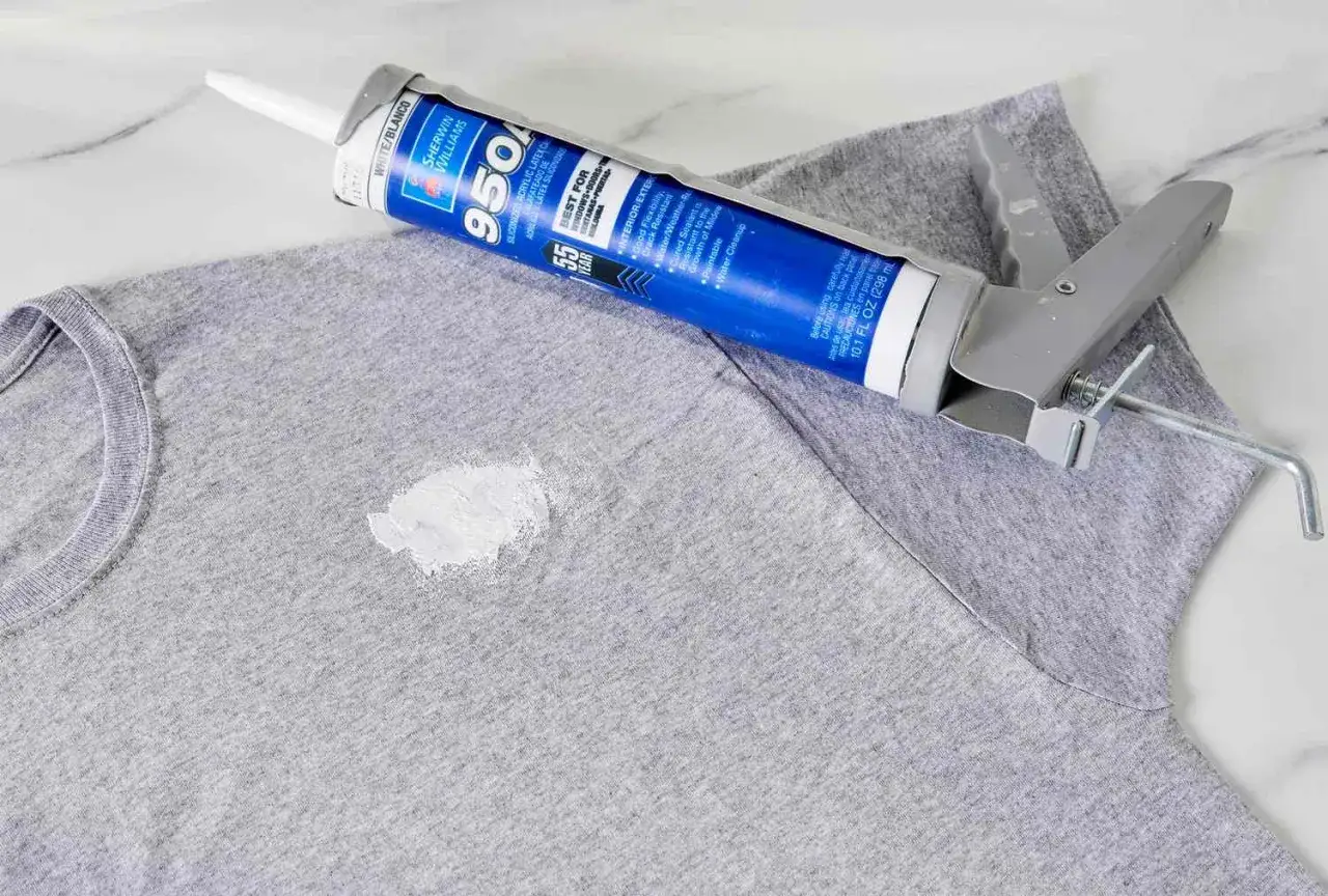 Tubo di silicone e pistola su maglietta grigia con macchia bianca. Guida su come togliere silicone dai vestiti.