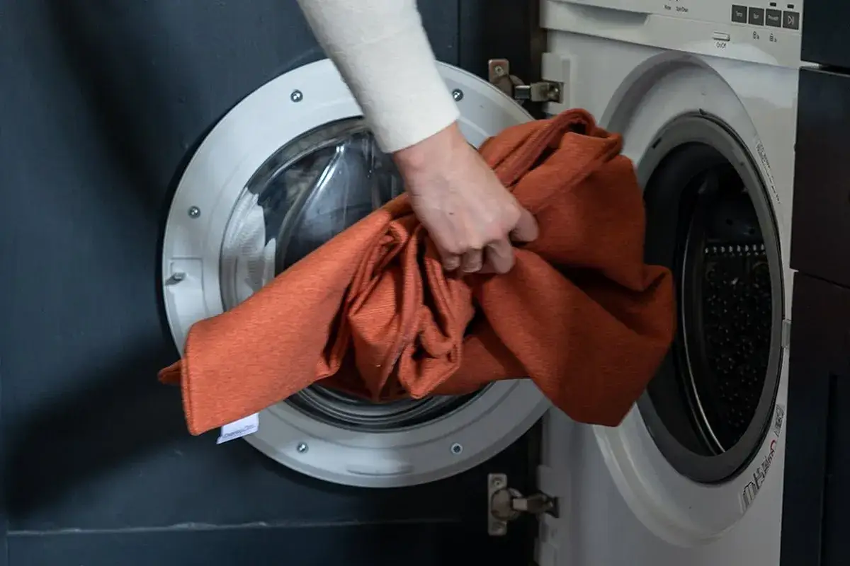 Una mano inserisce una cuccia arancione in lavatrice. Finalmente posso lavare la cuccia del cane in lavatrice per un cane felice e pulito.