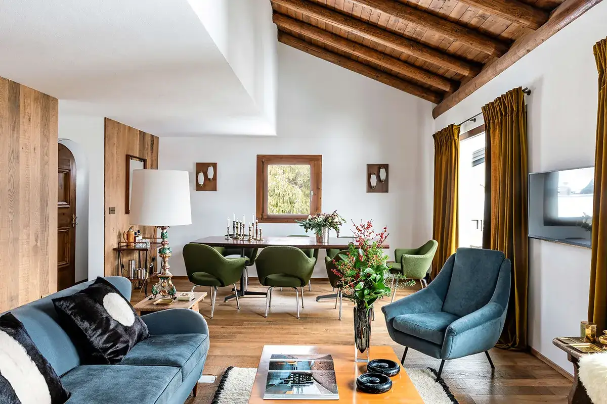 Soggiorno moderno con divano blu, poltrone verdi, tavolo da pranzo e travi a vista. Un esempio di ristrutturazione completa casa che unisce stile e comfort.