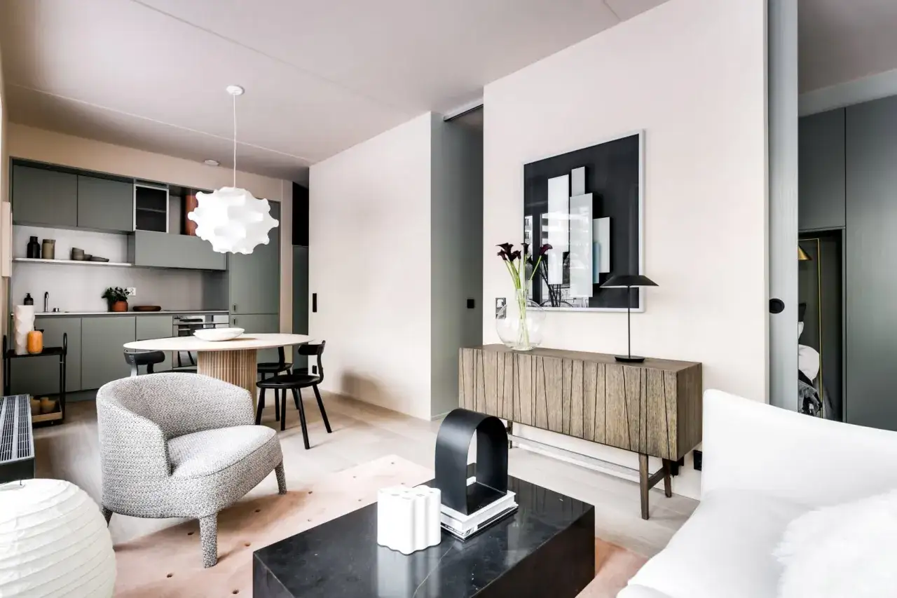 Soggiorno moderno con cucina a vista. Ottime idee arredo casa piccola: poltrona grigia, tavolino nero, credenza in legno e quadro astratto.