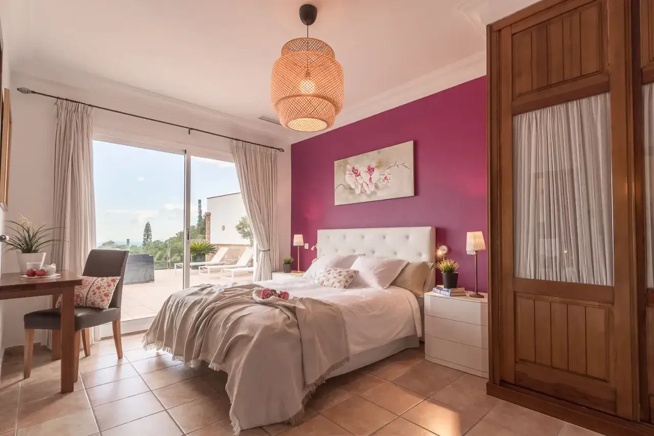 Camera da letto con parete magenta, un colore caldo e avvolgente. Letto bianco, armadio in legno e vista sulla terrazza.