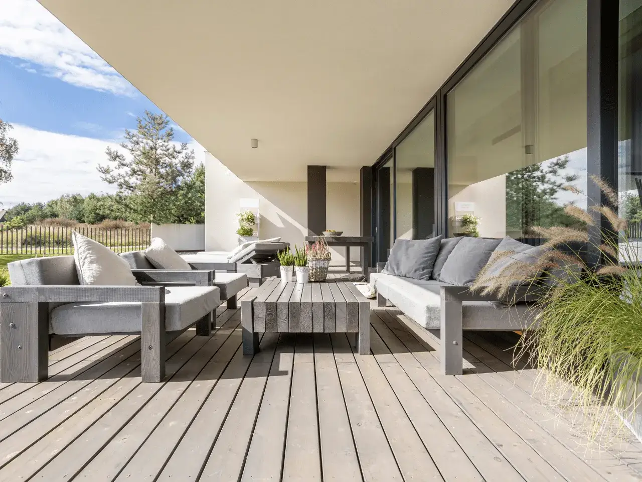 Arredare un piccolo terrazzo coperto con mobili moderni in legno grigio, divani comodi e un tavolino centrale.