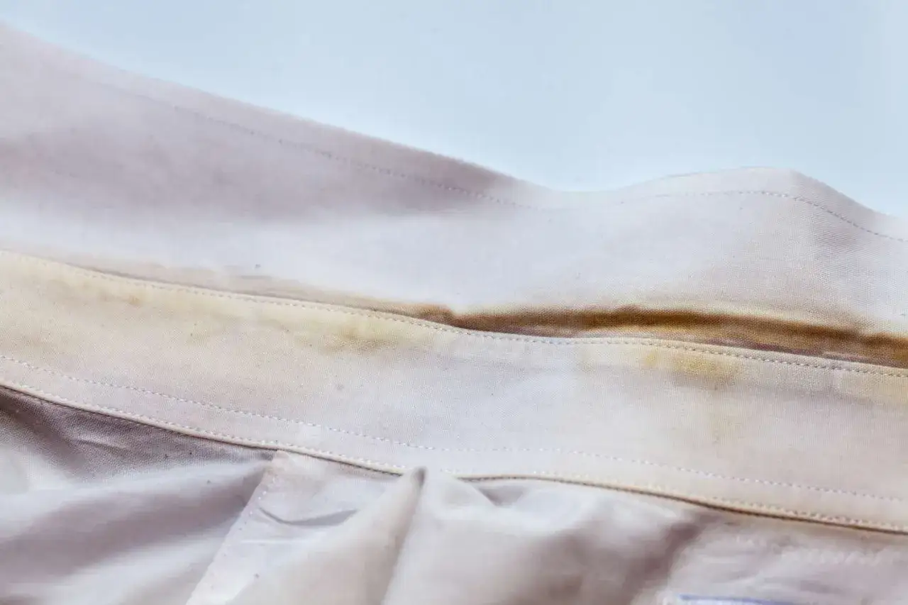 Colletto di camicia bianca con evidenti macchie gialle di candeggina, segno di un lavaggio errato.