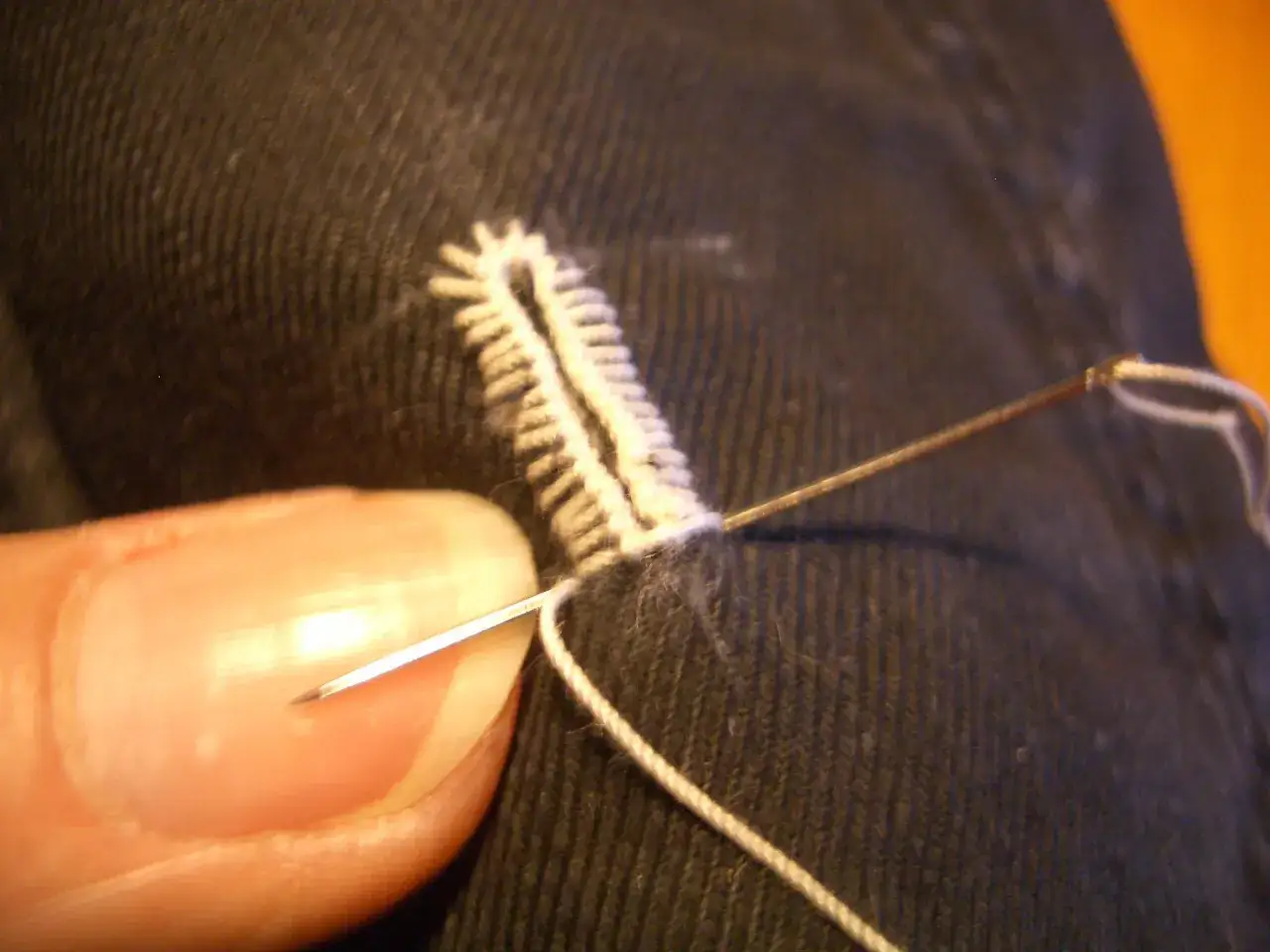 Dita e ago creano un punto occhiello a mano su tessuto scuro, un dettaglio di sartoria che richiede precisione.