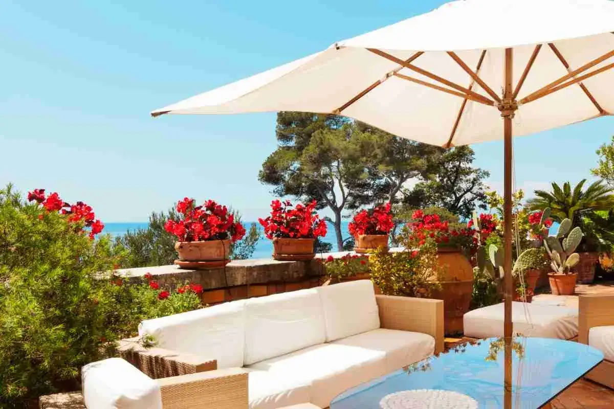 Un terrazzo come arredarlo: divani bianchi, piante rigogliose e un ombrellone creano un angolo relax con vista mare.