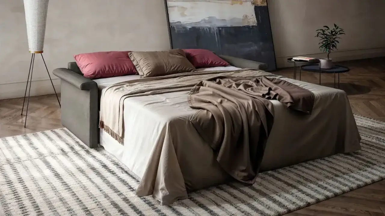 Un letto trasformabile in divano, con cuscini e coperte, ideale per chi cerca idee salvaspazio.