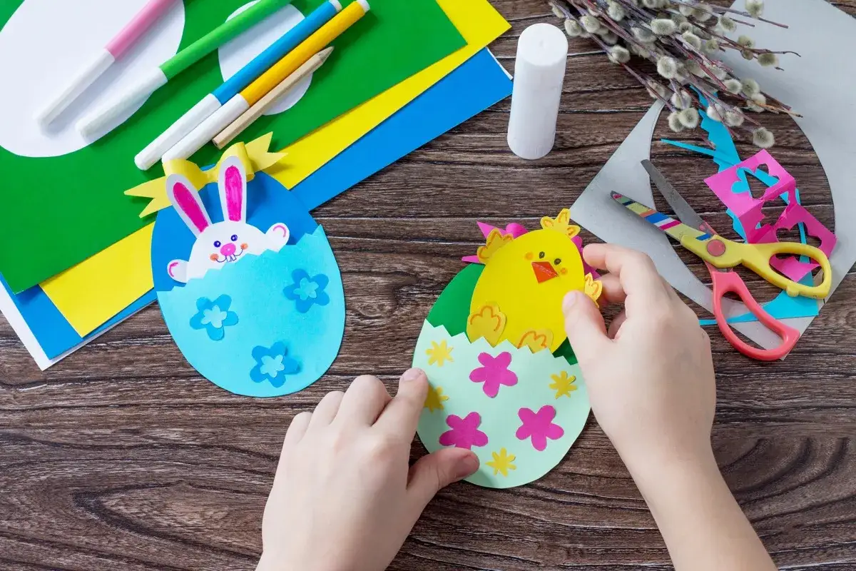 Bambini creano lavoretti di Pasqua scuola infanzia: un coniglietto e un pulcino escono da uova di carta colorate.