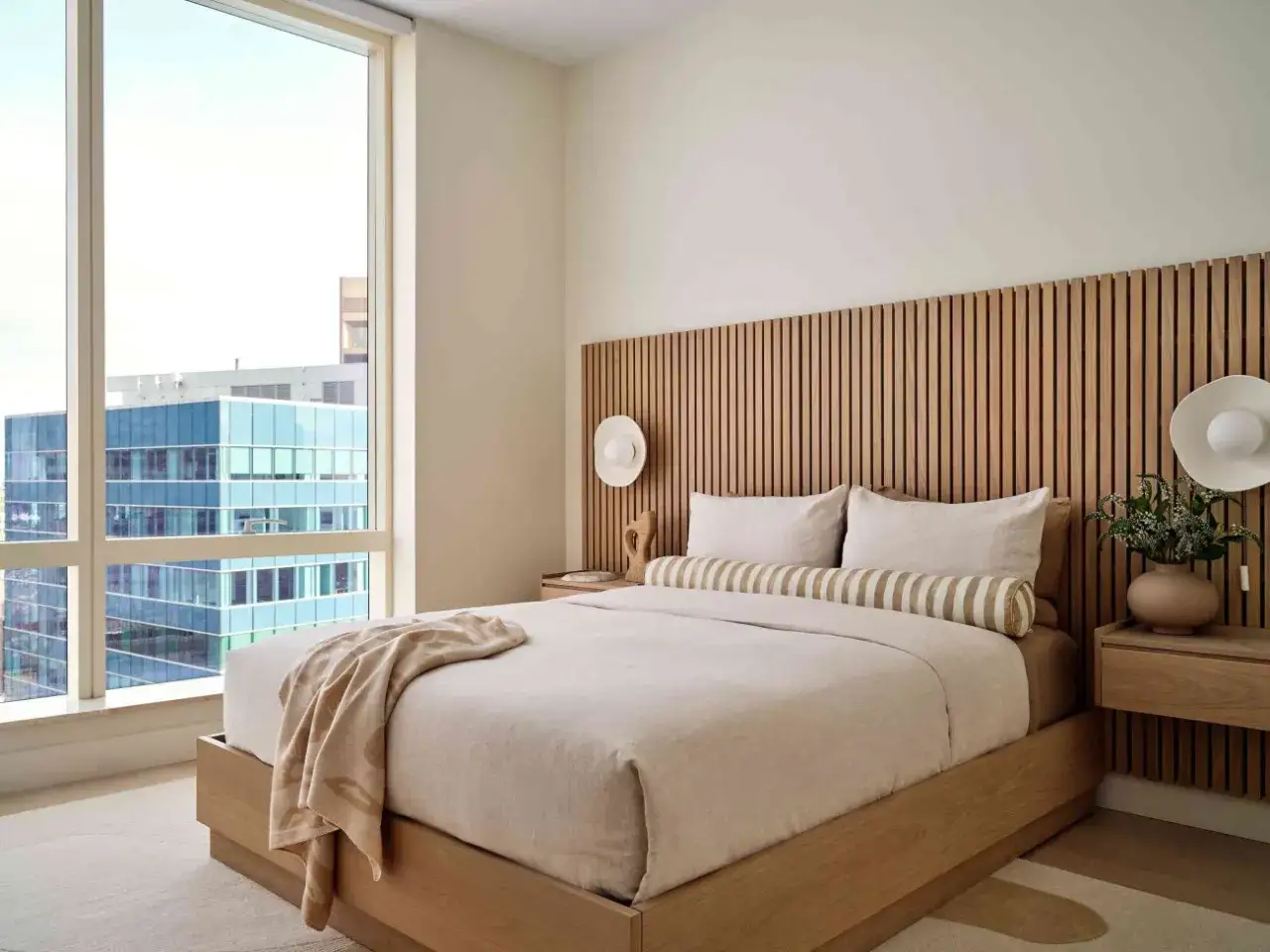 Camera da letto in stile giapponese con testiera in legno a listelli, letto king-size e vista sulla citt&agrave;.