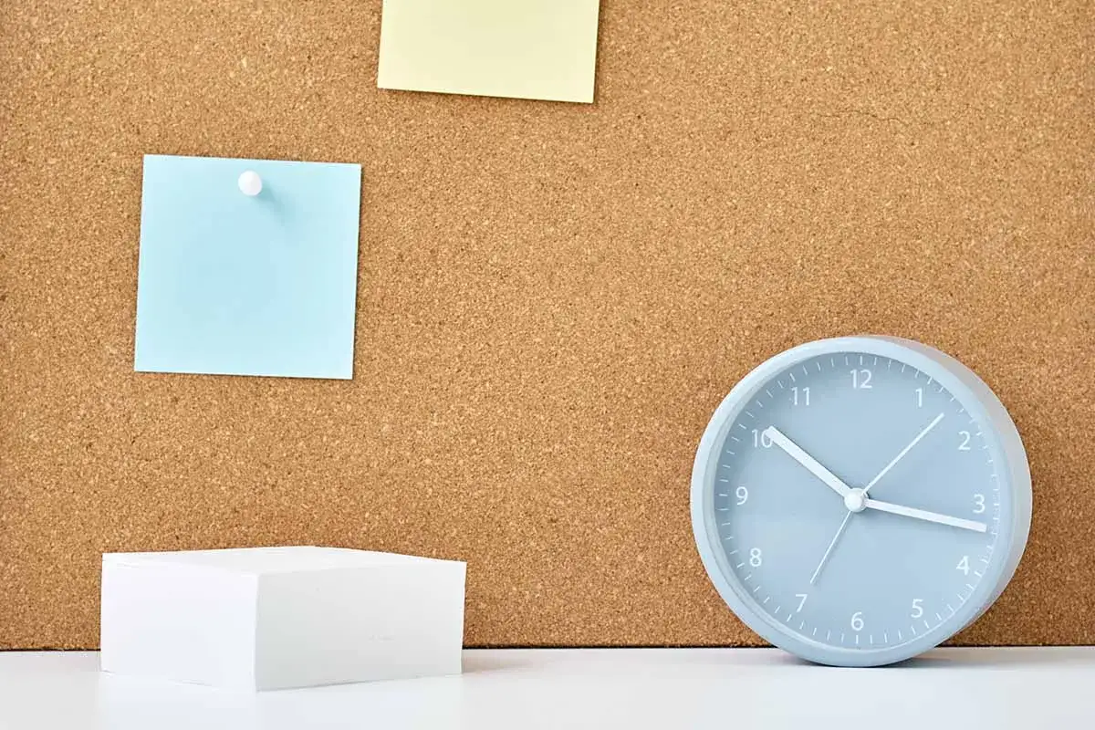 Bacheca fai da te con post-it blu e gialli, un blocco di fogli bianchi e un orologio azzurro.