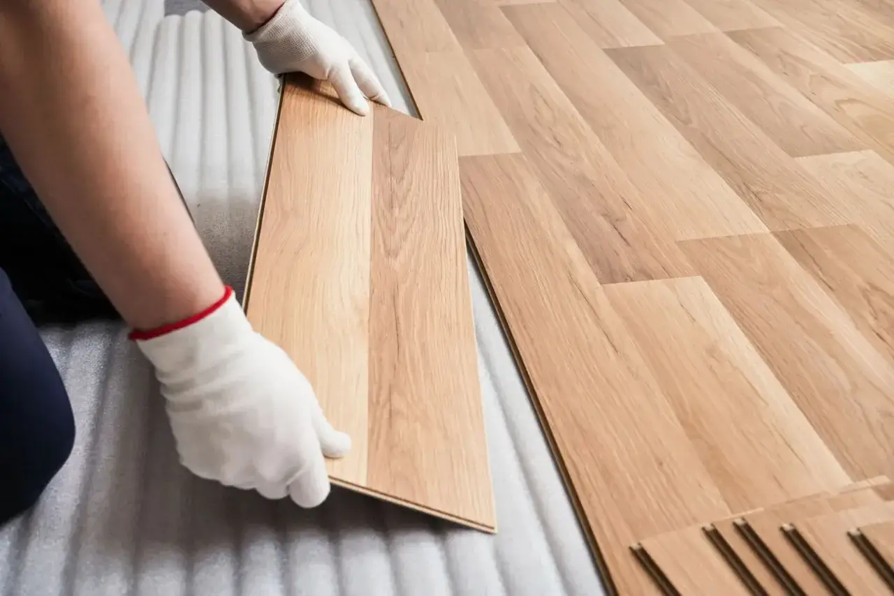Mani guantate posano una tavola di parquet laminato, mostrando lo spessore ideale per una posa fai-da-te.