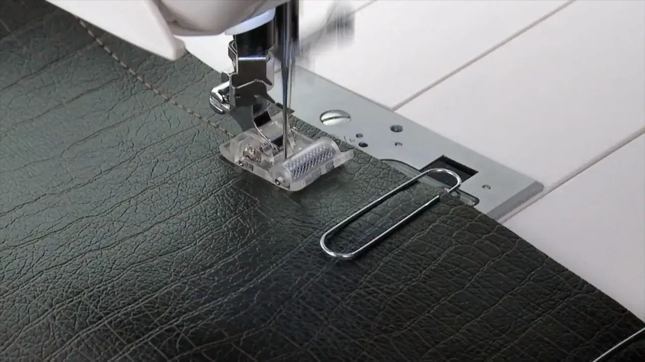 Macchina da cucire con piedino speciale per cucire la pelle. Un punto di cucitura è visibile sul materiale scuro.