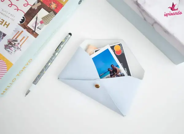 Pochette fai da te azzurra, con foto di coppia, carta di credito e banconota. Accanto, una penna e un libro.