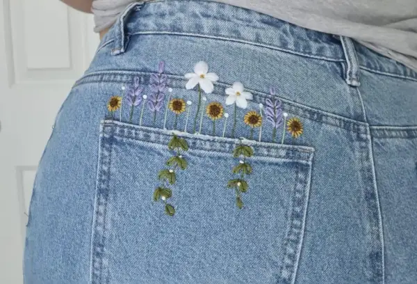 Top di jeans fai da te con ricamo floreale: lavanda, girasoli e margherite adornano la tasca posteriore, creando un look unico e primaverile.