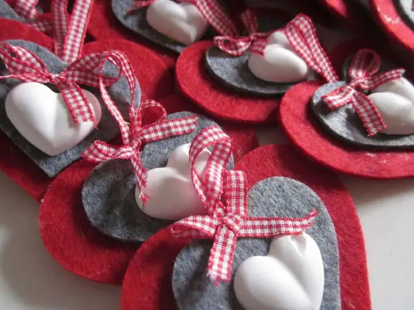 Cuori natalizi fai da te con feltro rosso e grigio, cuori bianchi e nastri a quadretti rossi.