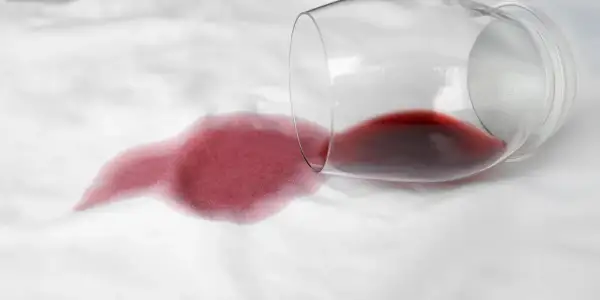 Calice di vino rosso rovesciato su tessuto bianco, creando una macchia. Come togliere macchie sconosciute e ostinate.