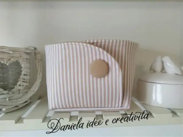Portaoggetti in stoffa da appendere fai da te, a righe beige e bianche, con bottone decorativo. Perfetto per organizzare piccoli oggetti.
