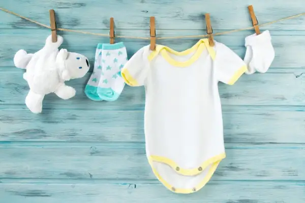 Vestiti da neonato bianchi e gialli appesi ad asciugare. Scopri come smacchiare i vestiti dei neonati ingialliti per mantenerli freschi.