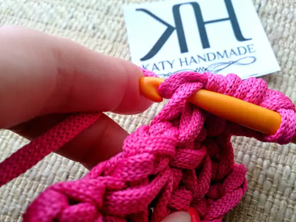 Mano che lavora all'uncinetto con filo rosa acceso, creando un punto pieno. Un tutorial su come ricamare una stella a punto pieno.