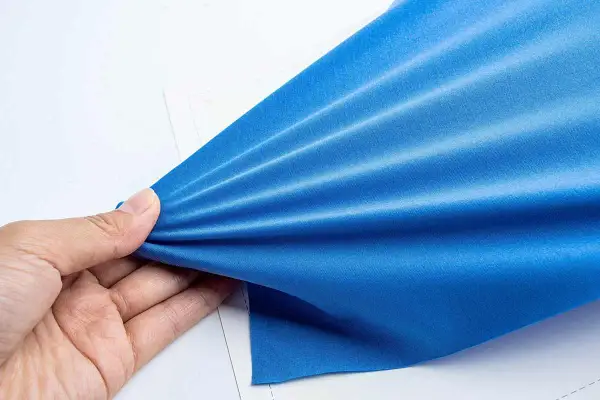 Mano che tiene un tessuto blu brillante, mostrando la sua elasticità e la trama del punto elastico a mano.