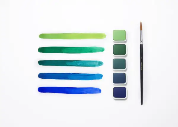 Pennellate verdi e blu mostrano la differenza tra colori acrilici e tempere, con pastiglie di colore e un pennello.