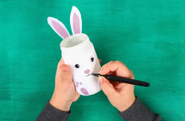 Mani che creano un coniglietto pasquale con un barattolo, perfetto per i lavoretti di Pasqua scuola infanzia.