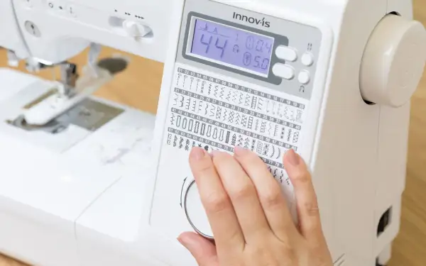 Dito, una mano seleziona tra i tanti punti macchina da cucire disponibili su un display digitale.