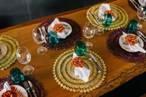 Sottopiatti eleganti fai da te con decorazioni floreali arancioni, bicchieri verdi e posate su un tavolo di legno.