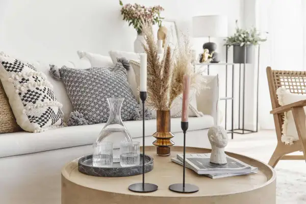 Tavolino rotondo con decanter, bicchieri, candele e scultura di testa. Cuscini decorativi e pampas sul divano creano un'atmosfera boho chic arredamento.