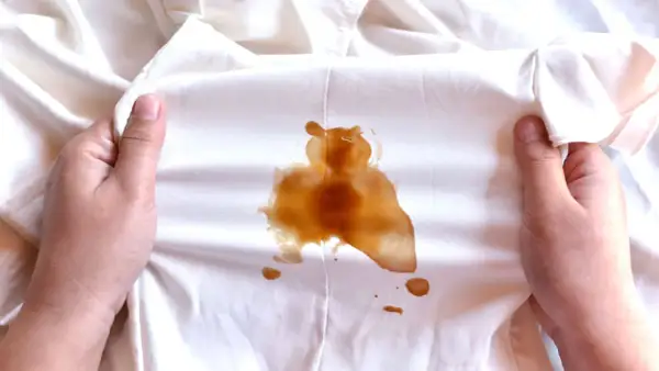 Mani che mostrano macchie di sapone marroni su un tessuto bianco.