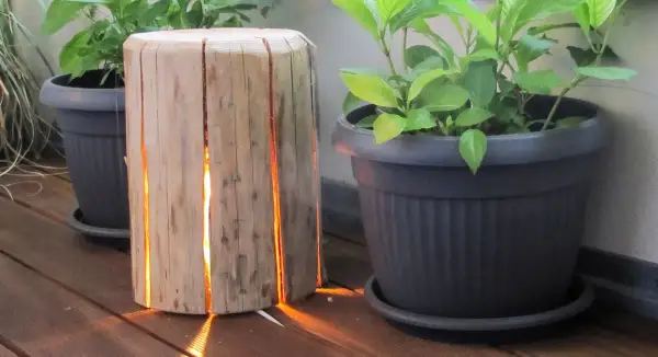 Lampada tronco legno fai da te illumina con calore il deck, creando un'atmosfera accogliente tra le piante in vaso.