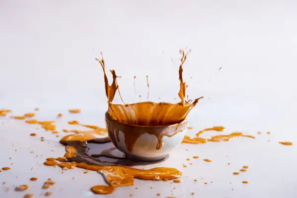 Schizzo di liquido marrone da una ciotola, creando macchie arancioni sui vestiti e sul tavolo.